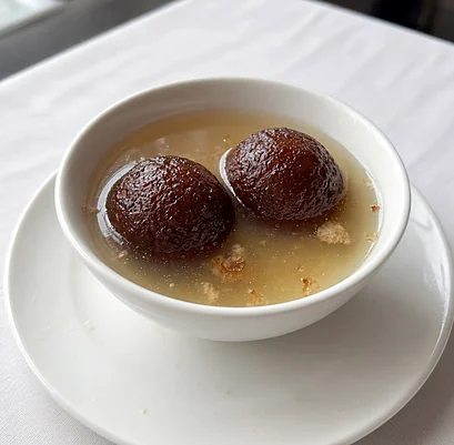 Two gulab jamun in syrup in a white bowl