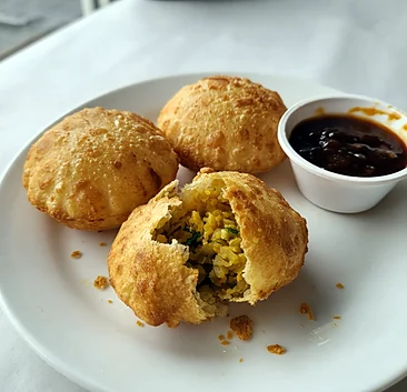 Three puris, one torn open to show the filling, with tamarind sauce