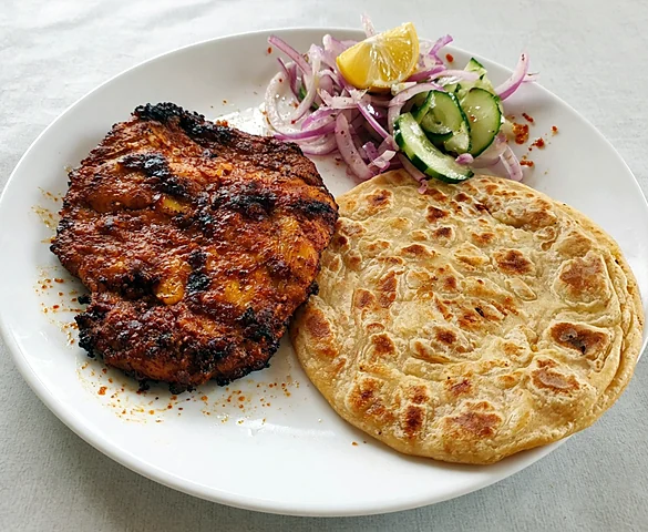 Chicken chaap with a paratha, onion and cucumber salad and a lemon wedge