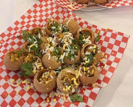 Fuchka with spiced chickpeas and potato in puffed shells, topped with grated egg and coriander, on checkered paper